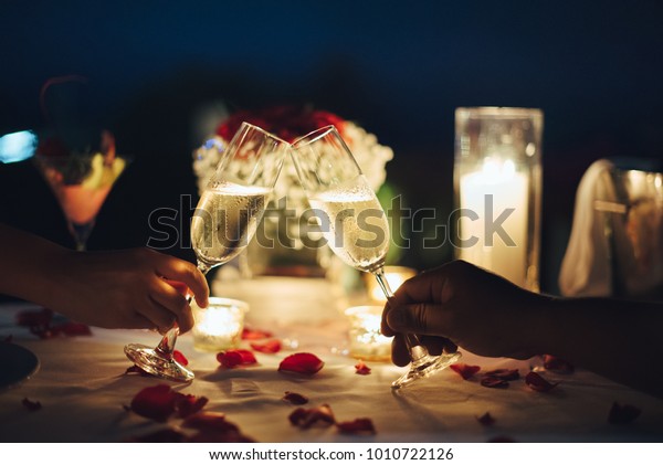 Romantic candlelight dinner for couple table setup\
at night. Man & Woman hold glass of Champaign. Concept for\
valentine\'s day or\
date.