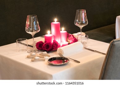 Romantic candlelit table setting for two with a centrepiece of burning red candles and fresh flowers set with matching red dinnerware and elegant glasses for Valentines