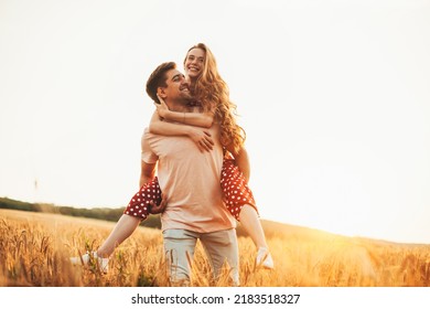 Romantic caucasian couple, man giving woman piggy back ride looking away standing in the wheat field together at sunset. Harvesting agriculture and plantation - Powered by Shutterstock