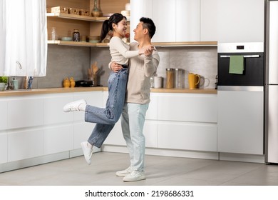 Romantic chinese lovers dancing waltz at kitchen, happy asian young lady enjoying time with her loving middle aged husband at home, cheerful man lifting up his beautiful wife, full length, copy space - Powered by Shutterstock