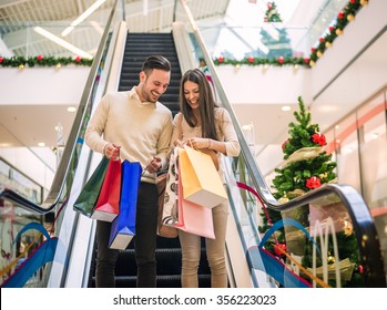 Romantic Christmas shopping.Sale, technology and people concept - happy young couple with shopping bags.Image taken inside a shopping mall.Selective focus