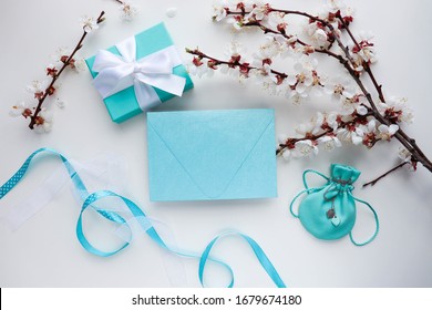romantic composition. gift box with bow, jewelry, flowering branch and envelope on a white background. congratulation. invitation