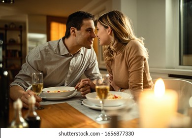 Romantic couple about to kiss while holding hands during dinner at dinning table. 