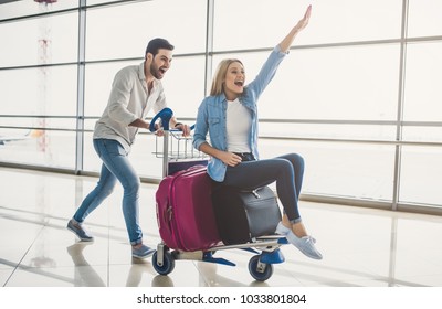 Romantic couple in airport. Attractive young woman and handsome man with suitcases are ready for traveling. Having fun on luggage trolley while waiting for departure.