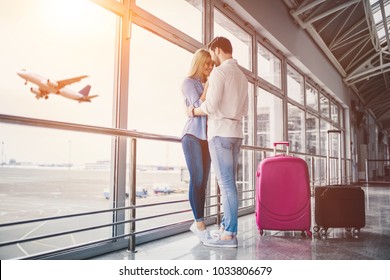 Romantic Couple In Airport. Attractive Young Woman And Handsome Man With Suitcases Are Ready For Traveling. Standing Near Panoramic Windows While Waiting For Departure.