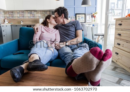 Romantic couple. Beautiful young loving couple embracing while sitting in big cozy sofa and watching TV at home.