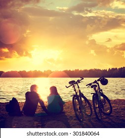 Romantic Couple with Bikes Relaxing at Sunset by the Lake. Fall in Love Concept. Toned Photo with Bokeh.