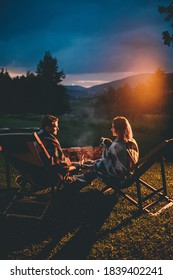 Romantic Couple With Cute Dog Relaxing In Campsite With Fire Pit. Burning Campfire with mountain landscape with night sky over the forest and hills. Getaway in wild nature. - Shutterstock ID 1839402241