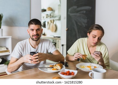 romantic couple eating breakfast at home, man using cell phone
