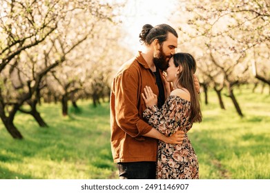 A romantic couple embraces in a blossoming orchard, surrounded by nature and sunlight in springtime - Powered by Shutterstock