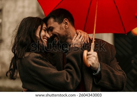 Romantic couple embracing and smiling under a red umbrella, enjoying a tender moment together on a rainy day, creating a warm and intimate atmosphere