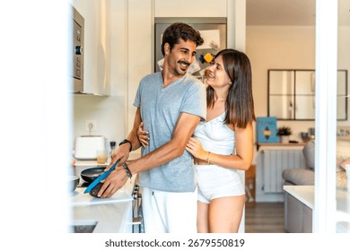 Romantic couple embracing while preparing a healthy breakfast together in a bright, modern kitchen, enjoying their morning routine
