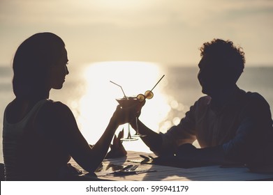 Romantic Couple Enjoy Sunset In Restaurant On The Beach Drinking Cocktails