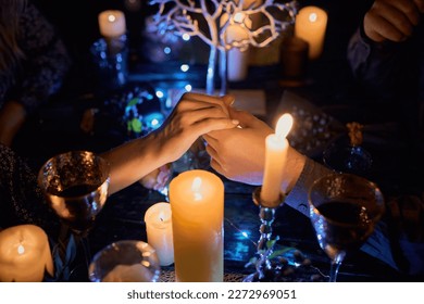 A romantic couple enjoying a candlelit dinner at a restaurant. The table is beautifully set and the dim lighting creates a cozy and intimate ambiance. The focus is on the couple's hands - Powered by Shutterstock