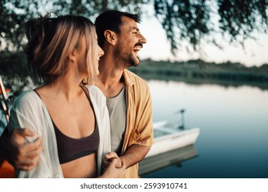 Romantic couple enjoying a peaceful moment by the lake, embracing and laughing together as the sun sets, creating a warm and intimate atmosphere