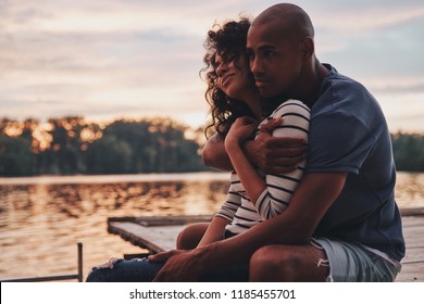 Romantic couple. Happy young couple embracing and smiling while sitting on the pier near the lake - Powered by Shutterstock