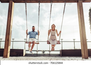 Romantic couple is having fun outside. Enjoying spending time together on a swings.
