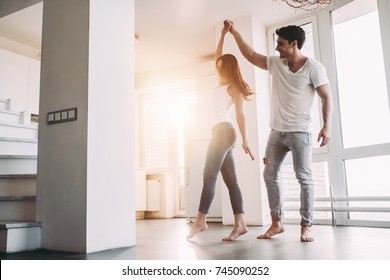 Romantic couple at home. Attractive young woman and handsome man are enjoying spending time together. Passionate couple is dancing on light modern kitchen with panoramic windows. - Shutterstock ID 745090252