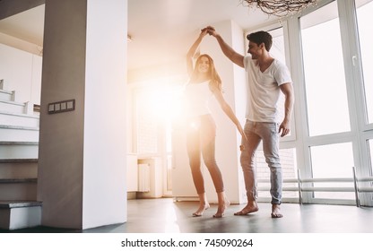 Romantic couple at home. Attractive young woman and handsome man are enjoying spending time together. Passionate couple is dancing on light modern kitchen with panoramic windows. - Powered by Shutterstock