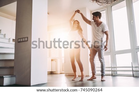 Romantic couple at home. Attractive young woman and handsome man are enjoying spending time together. Passionate couple is dancing on light modern kitchen with panoramic windows.