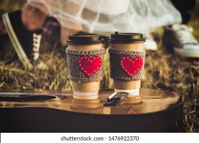 Romantic Couple Hugging While Having Picnic In Sunset Light. Coffee Cup Cozy Knitted Sleeve With Felt Red Heart.