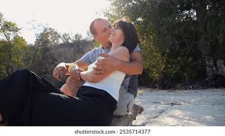 Romantic couple hugs during sitting on wooden log on the beach. Happy man kissing on cheek his beloved. Lovers spending time together at resort. Concept of vacation or holiday. Slow motion - Powered by Shutterstock