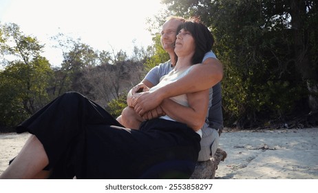 Romantic couple hugs during sitting on wooden log on the beach. Happy pair admiring a sea and landscape. Lovers spending time together at resort. Concept of vacation or holiday. Slow motion - Powered by Shutterstock