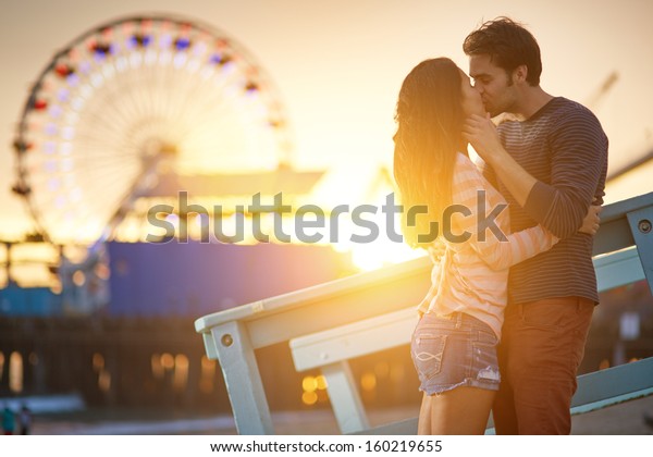 サンタモニカ観覧車の前の夕日にキスするロマンチックなカップル の写真素材 今すぐ編集