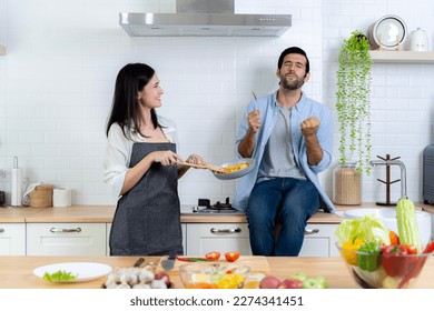 Romantic Couple At Kitchen. Man tasting food with good taste. Beautiful young wife cooking salad with smiling husband waiting for dinner or breakfast. Family enjoying weekend together. - Powered by Shutterstock