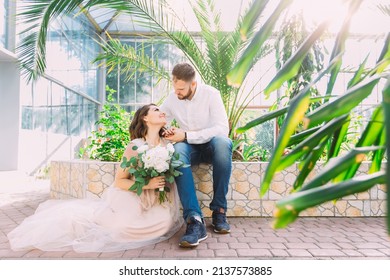 Romantic Couple Looks At Each Other In A Botanical Garden Near Greenery