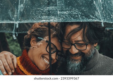 Romantic couple in love under umbrella in rainy day. Man and woman enjoy relationship and happiness together in winter autumn rain. Romance and people smiling end hugging at the park in leisure moment Stock Photo