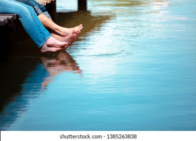 Romantic couple man and woman are sitting on a dock with barefoot feet dangling in pond water. Sunny weather. Happiness, vacation, summer, concept. Copy space for text.