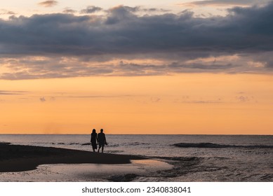 romantic couple of man and woman walking on sand beach at beautiful sunset