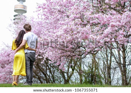 Romantic couple at Olympic park in Munich city, Germany on Spring season full of beautiful cherry blossom or Sakura flower. Happy family traveling concept.mixed race Asian-German Family woman and man.