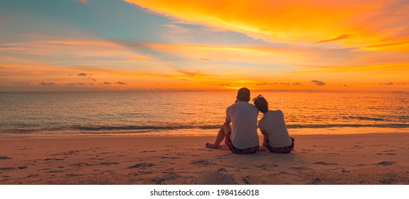 Romantic Couple On The Beach At Colorful Sunset On Background. Beautiful Tropical Sunset Scenery, Romance Couple Sitting And Watching The Sunset Sea And Sky, Horizon. Travel, Honeymoon Destination