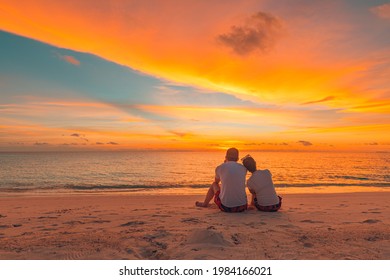 Romantic couple on the beach at colorful sunset on background. Beautiful tropical sunset scenery, romance couple sitting and watching the sunset sea and sky, horizon. Travel, honeymoon destination