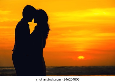 Romantic couple on the beach at colorful sunset on background