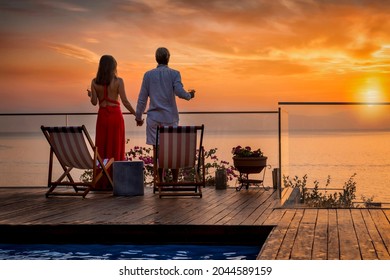 A romantic couple on summer vacation enjos the sunset over the mediterranean sea by the pool with a glass of wine - Powered by Shutterstock