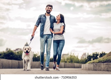 Romantic couple is on a walk in the city with their dog labrador. Beautiful young woman and handsome man are having fun outdoors with golden retriever labrador.