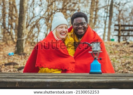 Romantic couple on winter vacation. A man and a woman are sitting together on a bench wrapped in blankets. The couple hugged and smiled.