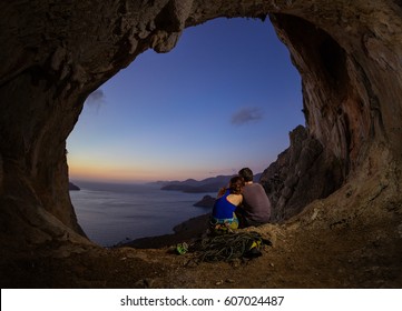 Romantic couple of rock climbers watching sunset from cave in cliff