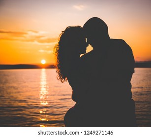 Romantic couple silhouettes on the beach, caressing each other with the sea and a beautiful colorful sunset in the background