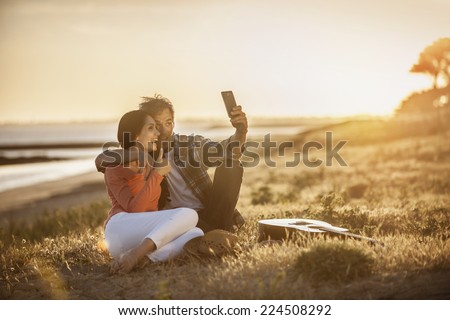 Romantic couple sitting on the beach at sunset and taking a selfie