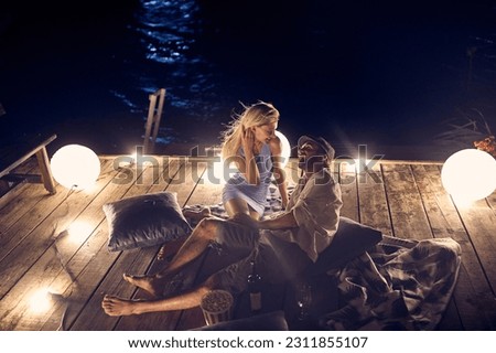 Romantic couple sitting together on a water dock at beautiful moon at night