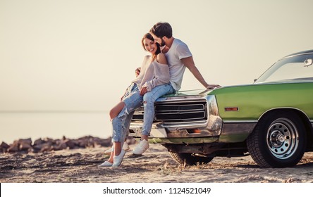 Romantic couple is standing near green retro car on the beach. Handsome bearded man and attractive young woman with vintage classic car. Love story.Muscle car