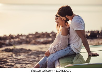 Romantic couple is standing near green retro car on the beach. Handsome bearded man and attractive young woman with vintage classic car. Love story.Muscle car