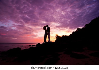 romantic couple standing on rocks by sea on purple dramatic sunset background - Powered by Shutterstock