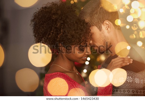 セーターを着たロマンチックなカップルが 大晦日に家で踊る クリスマス ボケの明かりの上に抱きしめる若い愛らしい男とアフリカの女性 金色の光に恋をして踊る多民族カップル の写真素材 今すぐ編集