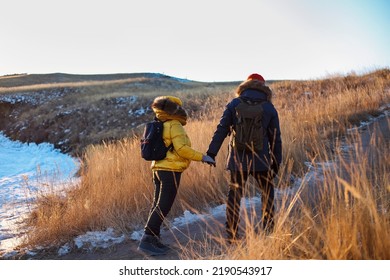 Romantic Couple Of Tourists Dressed In Warm Winter Sportswear With Tourist Backpacks Walking In The Snowy Mountains In An Incredible Sunset. Ogoi Island, Baikal Lake. Family, Rest.