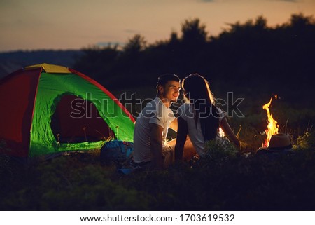 Romantic couple of tourists near the fire sit at to the camping.